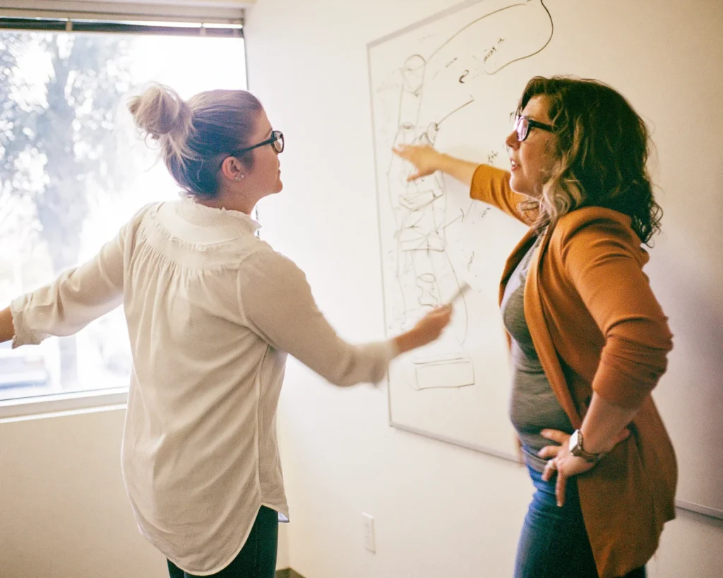 A consultant hands the whiteboard marker to a business owner stepping up to the board