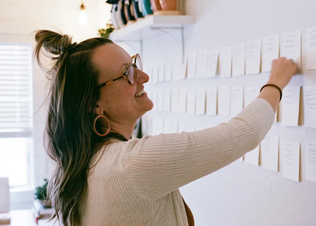 A smiling founder pins the next card onto a long wall of planning cards in her studio