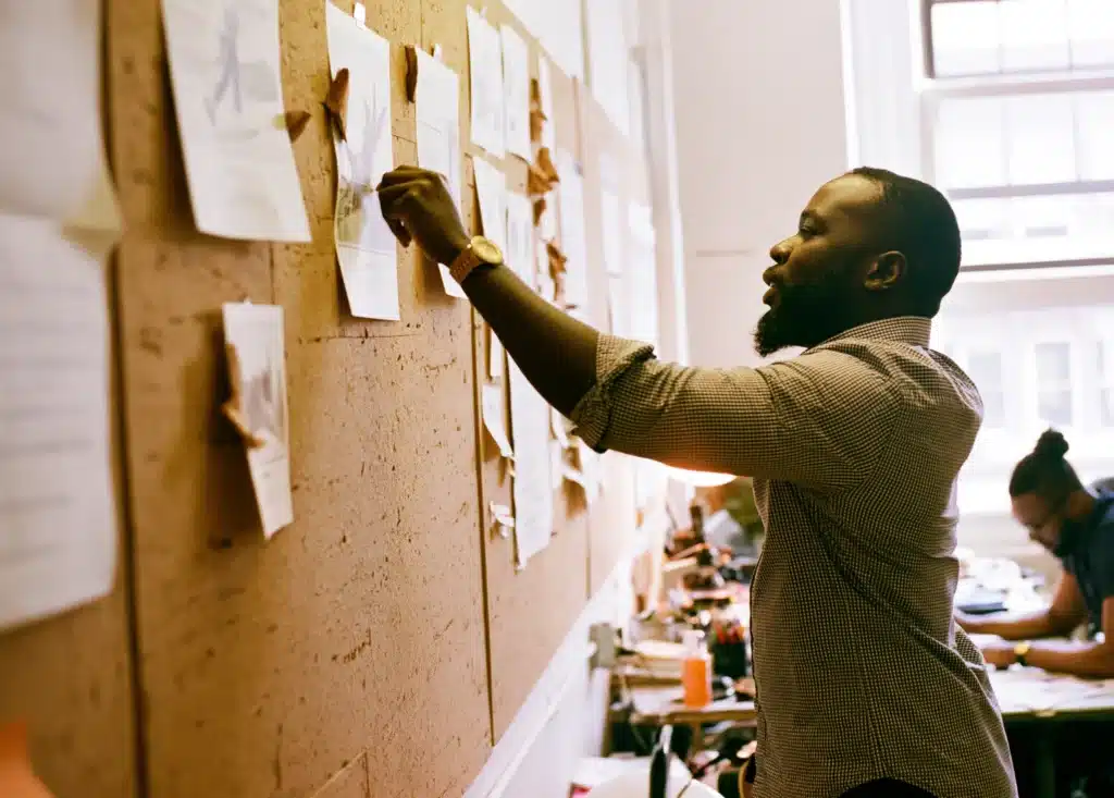 A founder rearranging priorities on a planning wall while his team works behind him