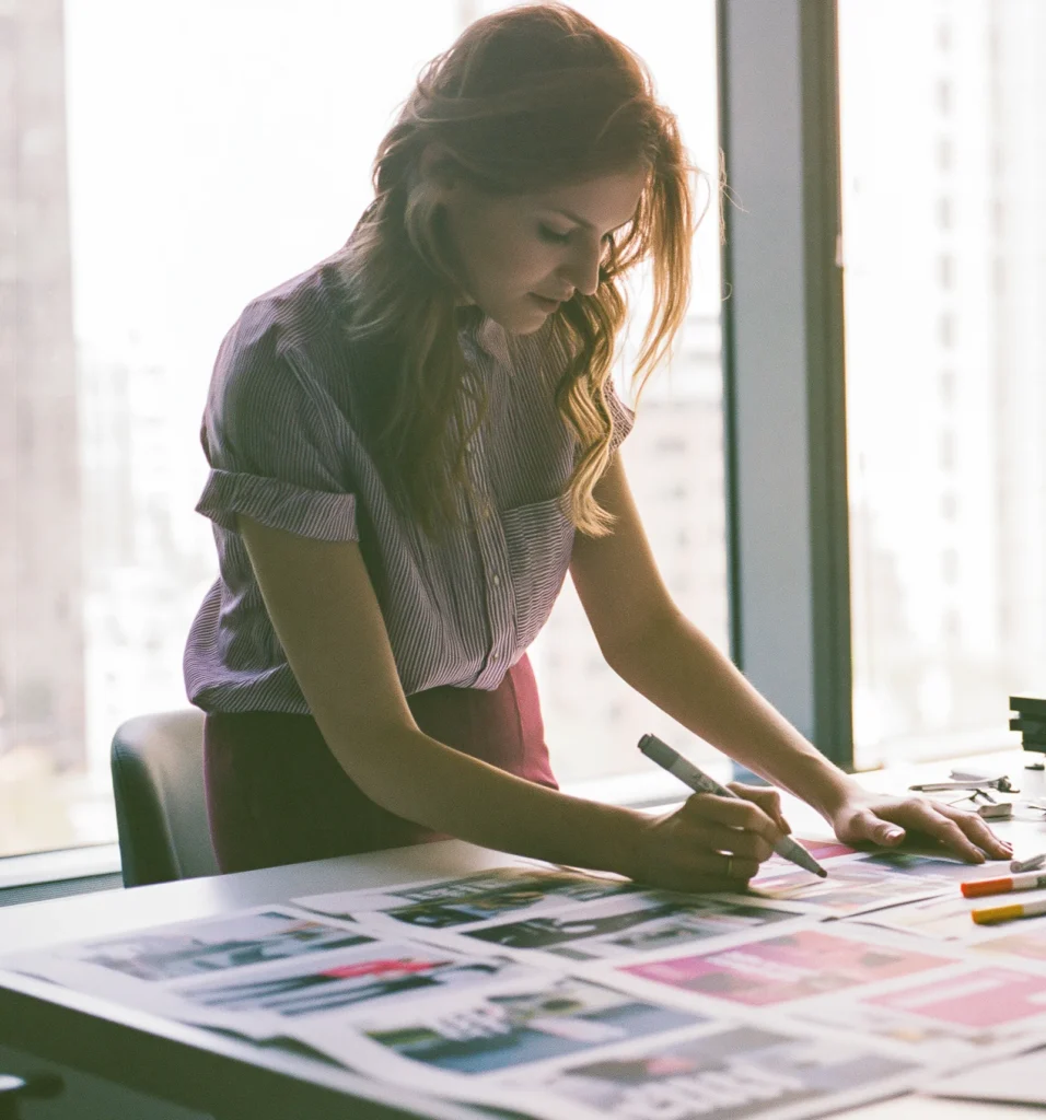 A marketer compares a grid of printed ad creatives laid out on a worktable