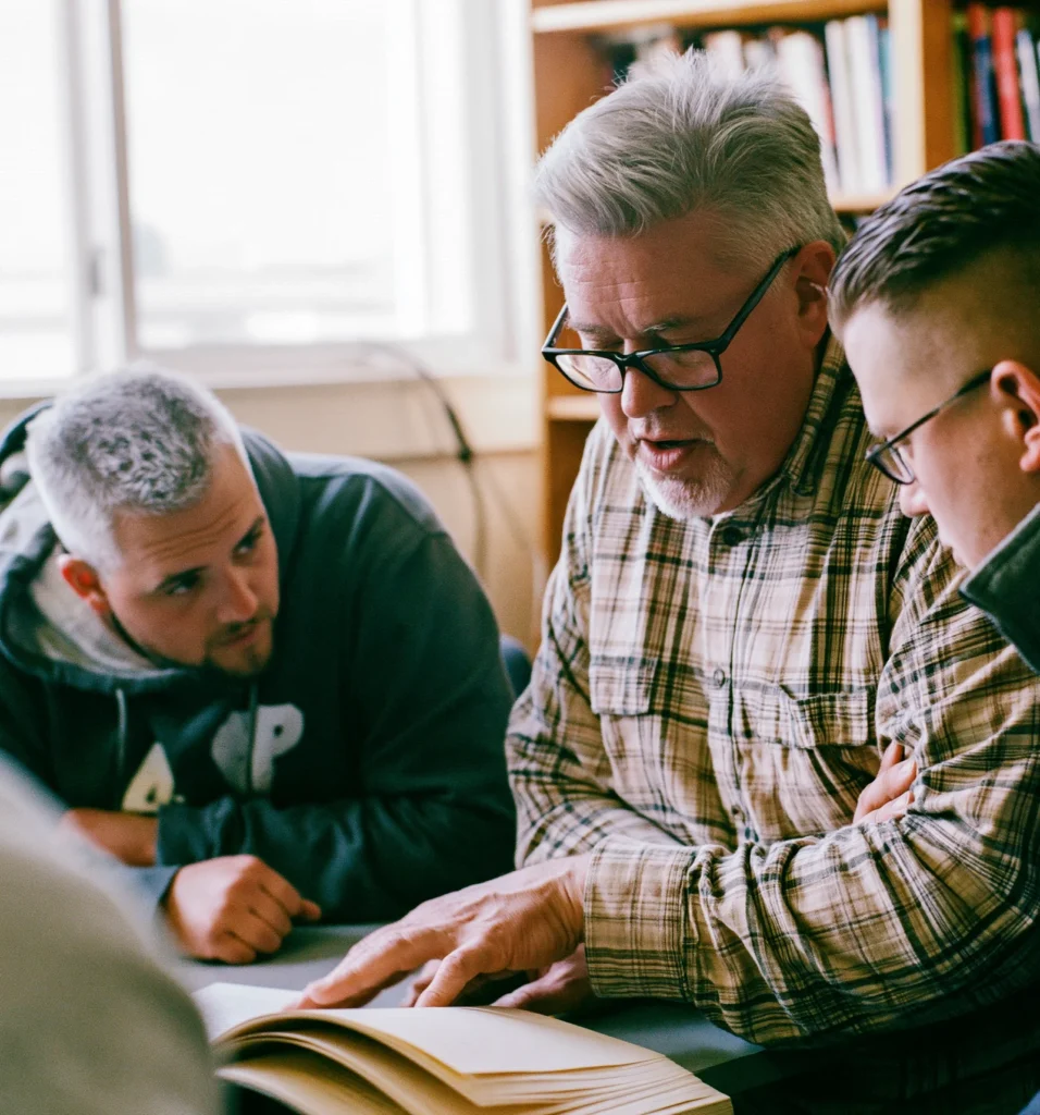 A mentor coaches a younger business leader over an open notebook at a small table