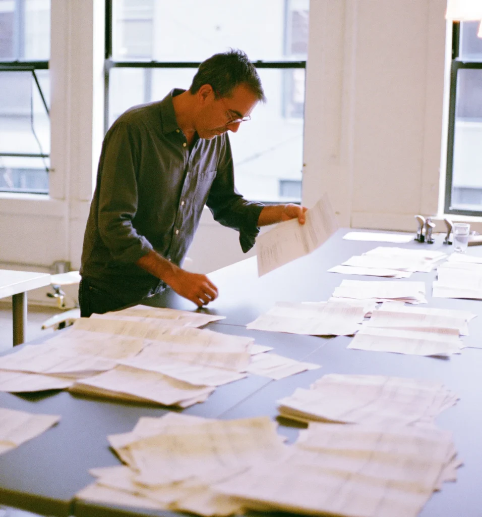 A researcher sorts printed customer survey sheets into clusters on a worktable