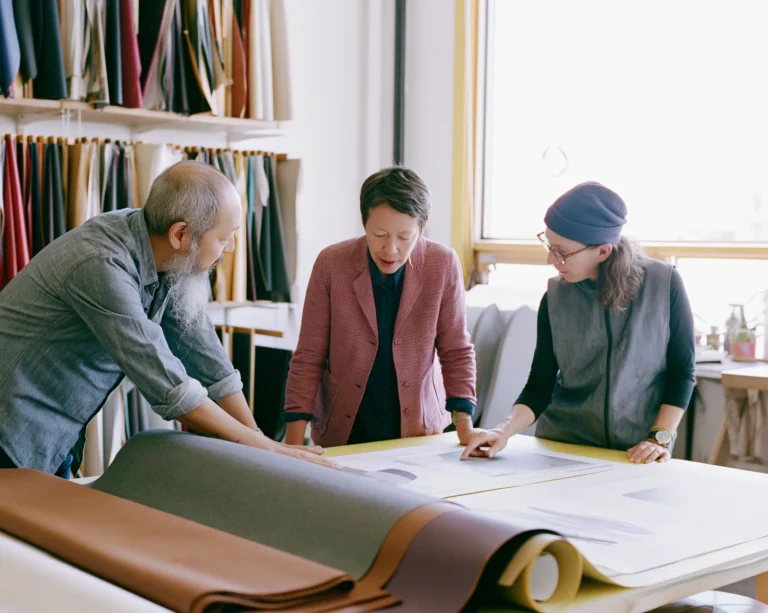 A team of specialists compares printed mockups around a studio worktable