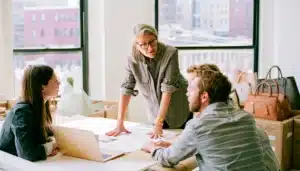 A woman leads two teammates through printed plans at a cluttered office table
